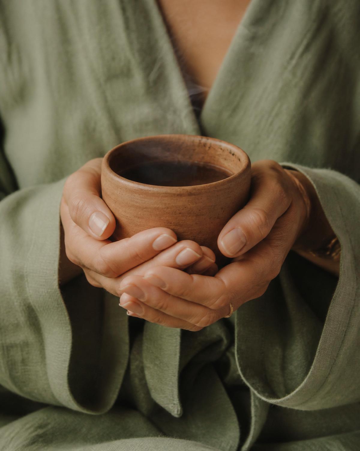 Hands cradling a warm terracotta cup